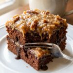 A close-up of a slice of German Chocolate cake with gooey topping and fudge filling, with a fork taking a bite.