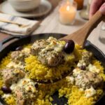 A close-up POV shot of a serving spoon scooping up hot, fluffy lemon rice, chicken, and melted feta from a skillet.