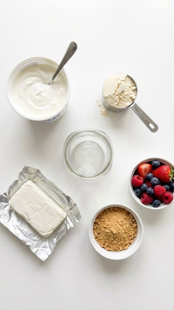A flat lay showing Greek yogurt, a scoop of protein powder, berries, and graham crackers.