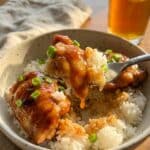 A close-up of a fork lifting a bite of sticky BBQ chicken and rice from a bowl.