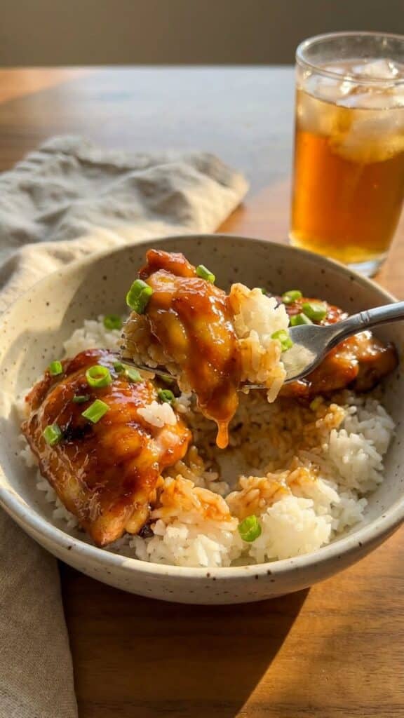 A close-up of a fork lifting a bite of sticky BBQ chicken and rice from a bowl.