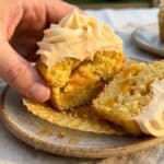 A close-up cross-section of a peach cupcake showing the moist crumb and fruit pieces inside, topped with frosting.