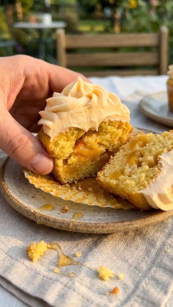 A close-up cross-section of a peach cupcake showing the moist crumb and fruit pieces inside, topped with frosting.