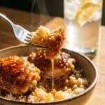 A close-up of a fork lifting a bite of sticky hot honey chicken and rice.