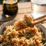 A close-up of chopsticks lifting steaming chicken fried rice from a bowl.