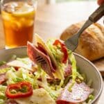 A close-up of a fork lifting a bite of chopped salad with salami, cheese, and lettuce.