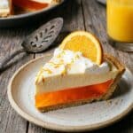A close-up side view of a slice of orange creamsicle pie showing the fluffy mousse texture on a plate.