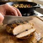 A close-up of a knife slicing a chicken breast, showing a juicy white interior and golden crust.