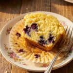 An overhead flat lay view of baking ingredients including fresh blueberries, lemons, flour, sugar, butter, and a muffin tin.