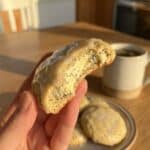 A close-up of a hand holding a bitten lemon cookie, showing the soft, dense interior texture.