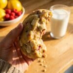 A flat lay showing lemon zest, fresh raspberries, white chocolate chips, flour, and butter on a wooden board.