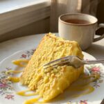 A close-up of a slice of lemon velvet cake on a plate, with a fork lifting a moist bite covered in frosting.