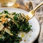 A close-up of a fork lifting a bite of kale salad with cheese and crumbs, showing the tender texture.
