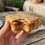 A close-up of a hand holding a strawberry lemon blondie with a bite taken out, showing the chewy texture and juicy fruit inside.