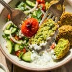 A close-up of a fork lifting a crispy falafel dipped in sauce with fresh vegetables.
