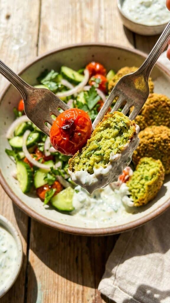 A close-up of a fork lifting a crispy falafel dipped in sauce with fresh vegetables.
