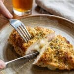 A close-up POV shot of a knife cutting into parmesan crusted chicken, revealing a creamy cheese layer under the crust.