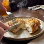 A close-up POV shot of a knife cutting into parmesan crusted chicken, revealing a creamy cheese layer under the crust.