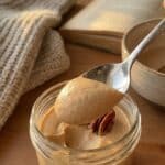 A close-up of a spoon holding smooth maple mousse with a pecan, showing the creamy texture.