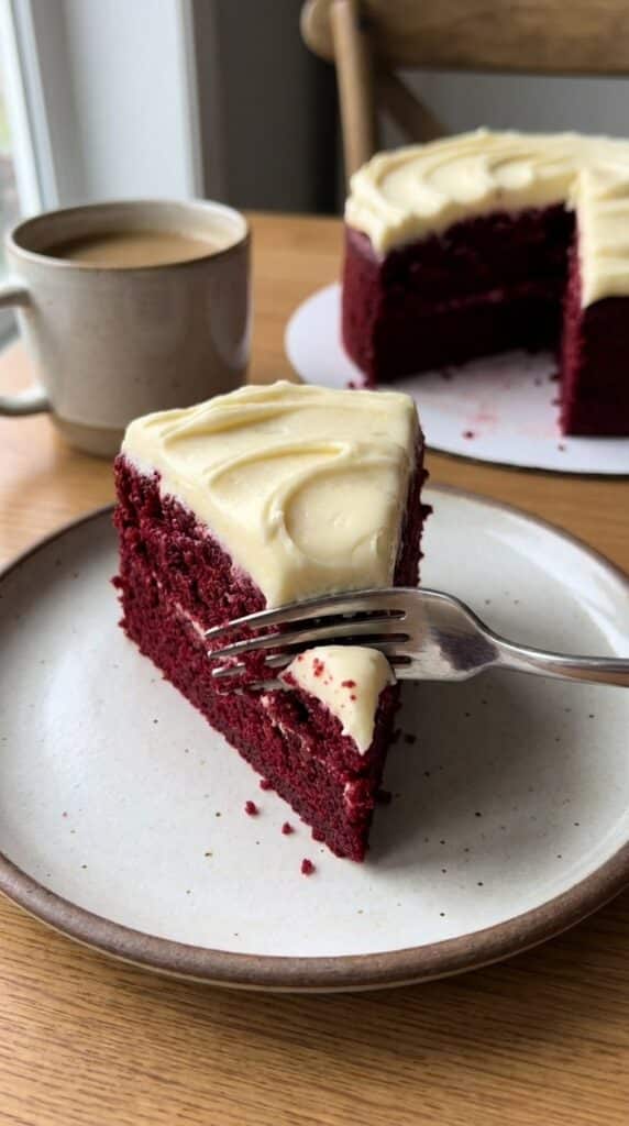 A close-up of a fork cutting into a slice of moist red velvet cake with thick cream cheese frosting.