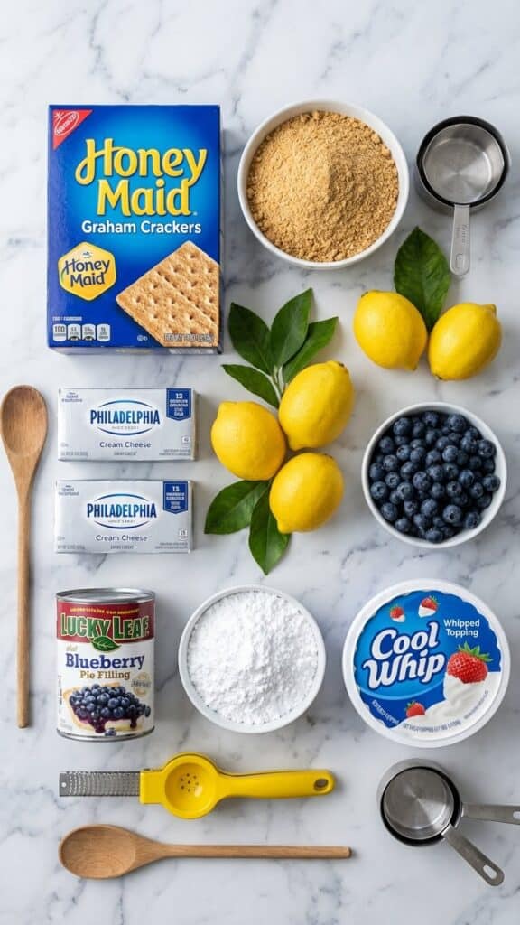 A flat lay showing graham crackers, lemons, cream cheese, blueberries, and whipped topping on a marble counter.