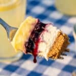 A close-up of a fork taking a bite of creamy lemon blueberry dessert.