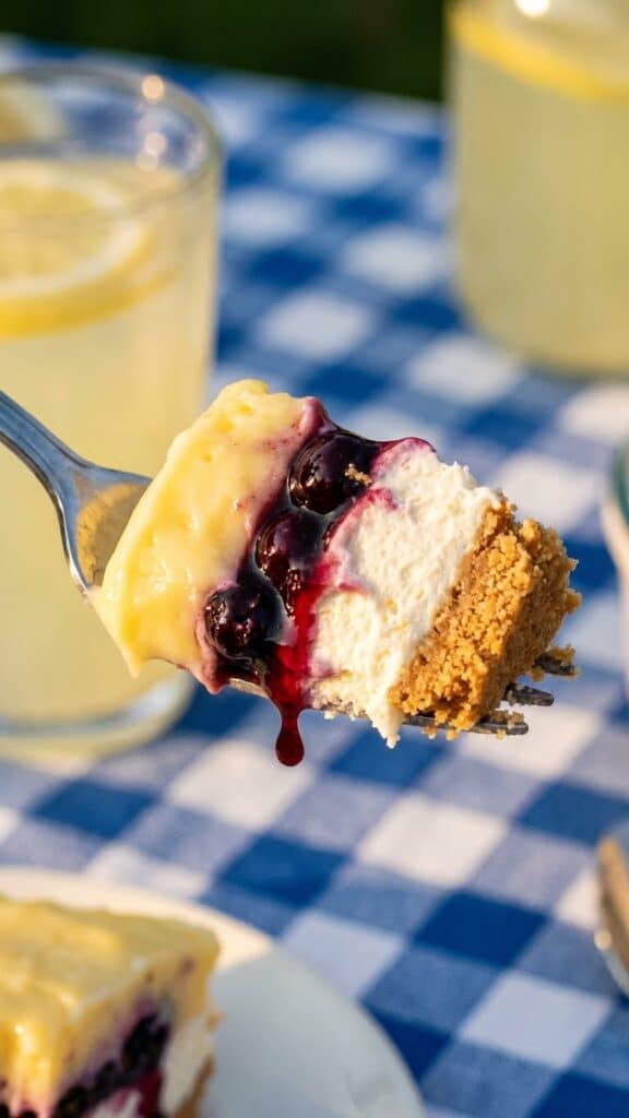 A close-up of a fork taking a bite of creamy lemon blueberry dessert.