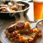 A close-up of a fork lifting a piece of browned sausage and seasoned rice from a plate.