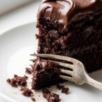 A close-up macro shot of a fork sliding into a moist slice of dark chocolate cake.