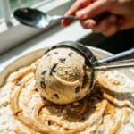 A close-up of an ice cream scoop rolling a ball of peanut butter ice cream from a container.
