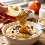 A close-up of an apple slice dipping into thick peanut butter mousse.