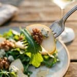 A close-up of a fork lifting a bite of pear, walnut, cheese, and lettuce.