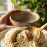 A close-up of a gold spoon lifting a bite of creamy pistachio ice cream with visible nuts.