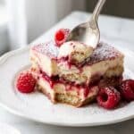 An overhead flat lay view of ingredients including ladyfingers, mascarpone, cream, and fresh raspberries.