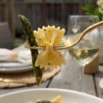 A close-up of a fork lifting a bite of bowtie pasta and roasted asparagus.