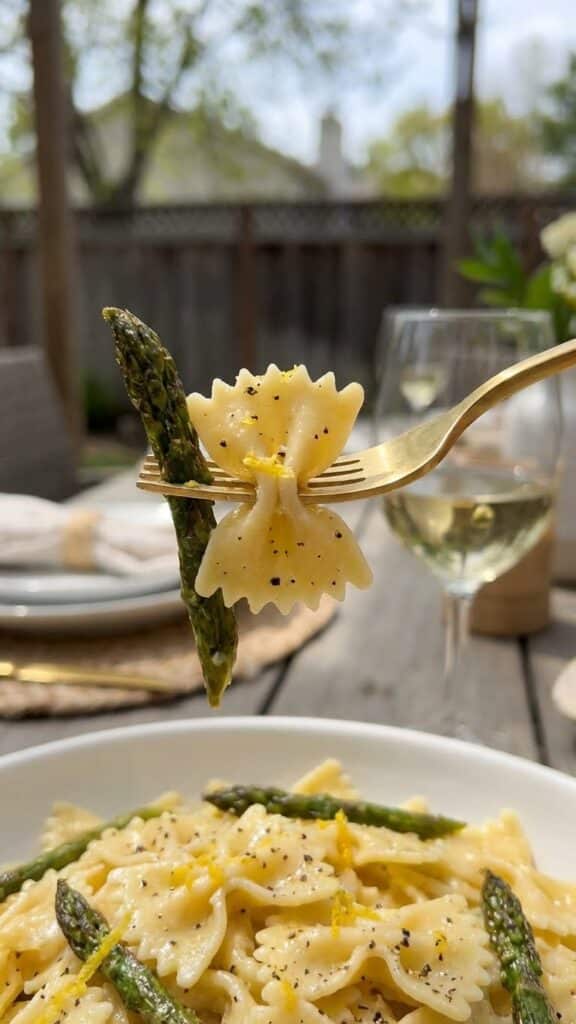 A close-up of a fork lifting a bite of bowtie pasta and roasted asparagus.