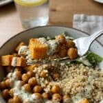 A close-up of a fork lifting a bite of roasted chickpeas and sweet potatoes with creamy dressing.