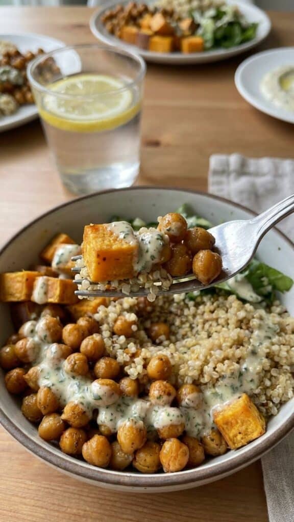 A close-up of a fork lifting a bite of roasted chickpeas and sweet potatoes with creamy dressing.