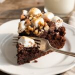 A close-up of a slice of rocky road cake on a plate with a fork taking a bite, showing the moist crumb and toppings.
