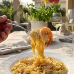 A close-up POV shot of a fork lifting a bite of creamy shrimp orzo with a hand squeezing fresh lemon juice over it.