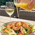 A close-up of lemon vinaigrette being poured over a shrimp and artichoke salad.