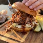 A close-up of a large BBQ pulled pork sandwich topped with coleslaw on a wooden board.