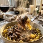 A close-up of a fork lifting tender beef and noodles covered in creamy stroganoff sauce from a bowl.