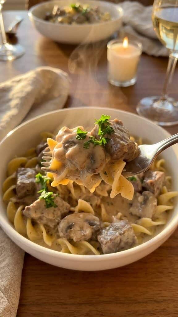 A close-up of a fork lifting creamy beef stroganoff and egg noodles from a bowl