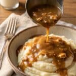 A close-up of a ladle pouring savory chicken and gravy over mashed potatoes.