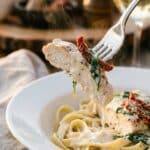 A close-up of a fork lifting a piece of creamy chicken with spinach and sun-dried tomatoes over pasta.