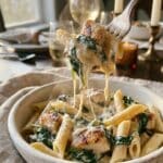 A close-up of a fork lifting creamy penne pasta, chicken, and spinach from a bowl.