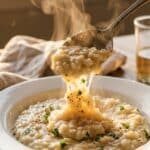 A close-up of a spoon lifting creamy risotto, showing the thick texture and steam rising.
