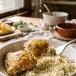 A close-up of a fork lifting tender chicken and rice from a bowl, with fresh lemon juice being squeezed over it.
