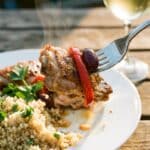 A close-up of a fork lifting a piece of chicken with an olive and pepper, served over quinoa.
